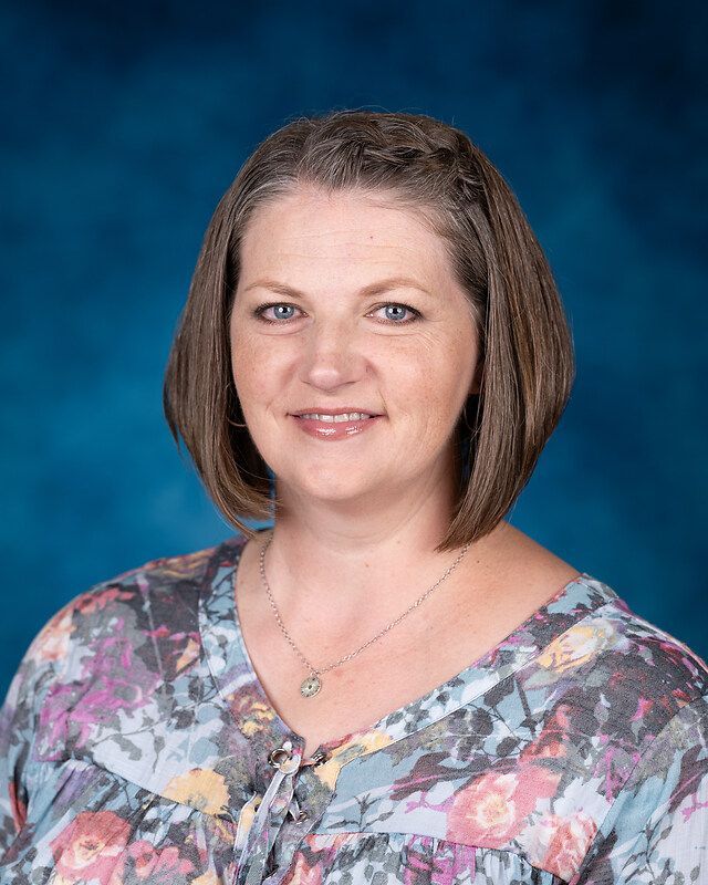 A woman in a floral shirt and necklace is posing for a picture.