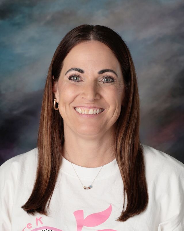 The woman is wearing a pink sweater and smiling for the camera.