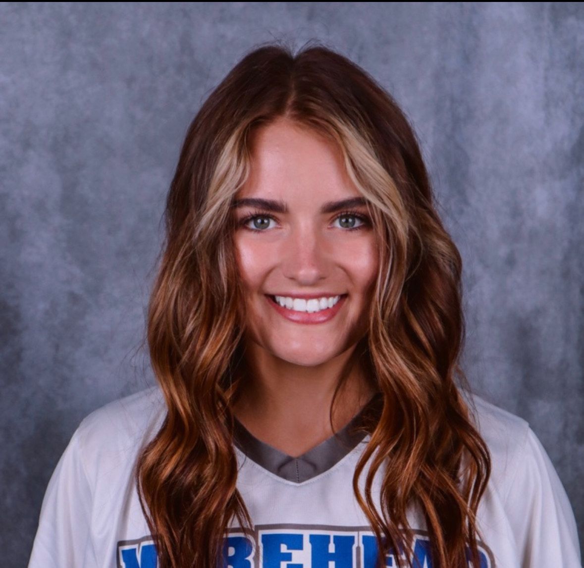 A woman wearing a plaid shirt and a necklace is smiling for the camera.