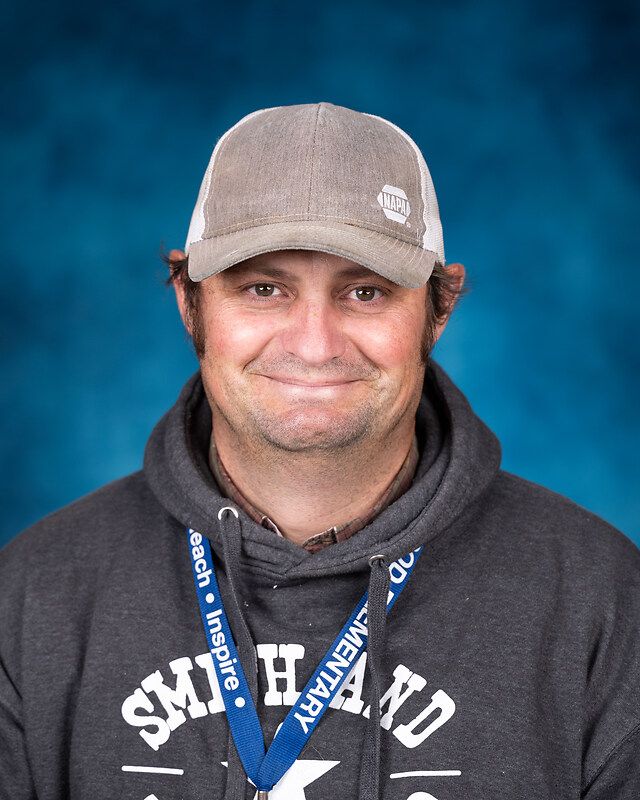 A man wearing a hat and a lanyard is smiling for the camera.