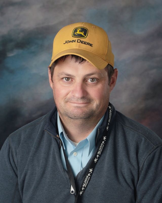 A man wearing a hat and a lanyard is smiling for the camera.