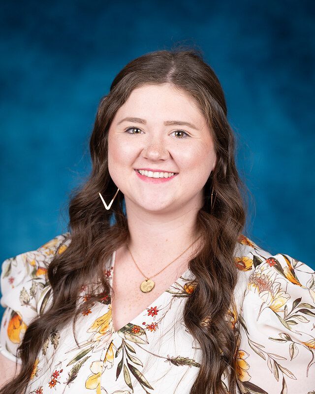 A woman in a floral shirt and necklace is smiling for the camera.
