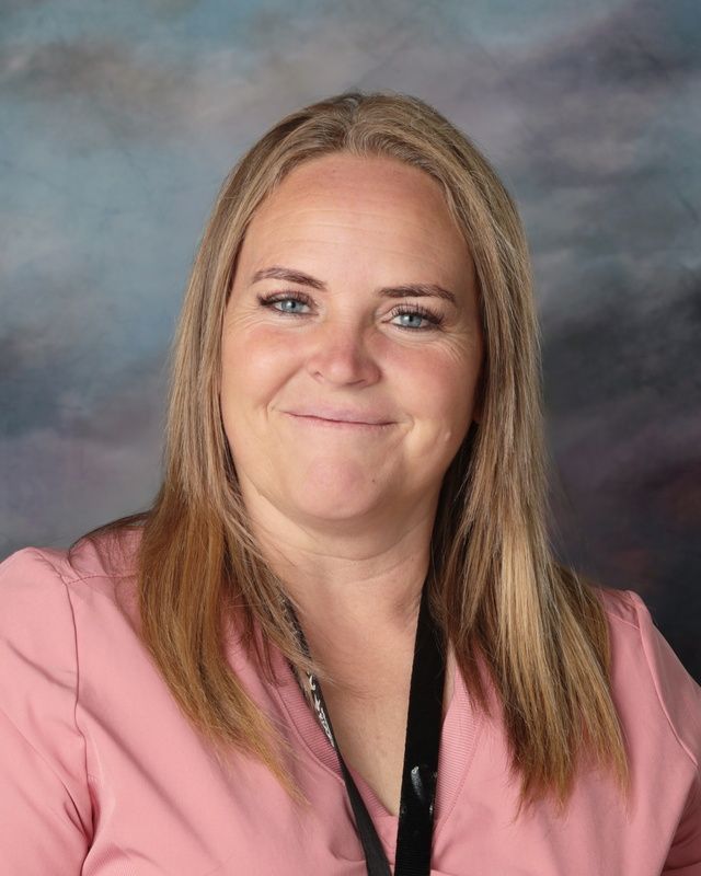 A woman in a pink shirt and earrings is smiling for the camera.
