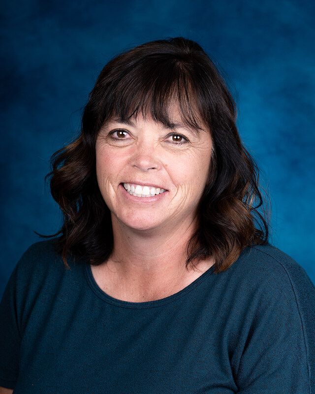 A woman is smiling for a picture in front of a blue background.
