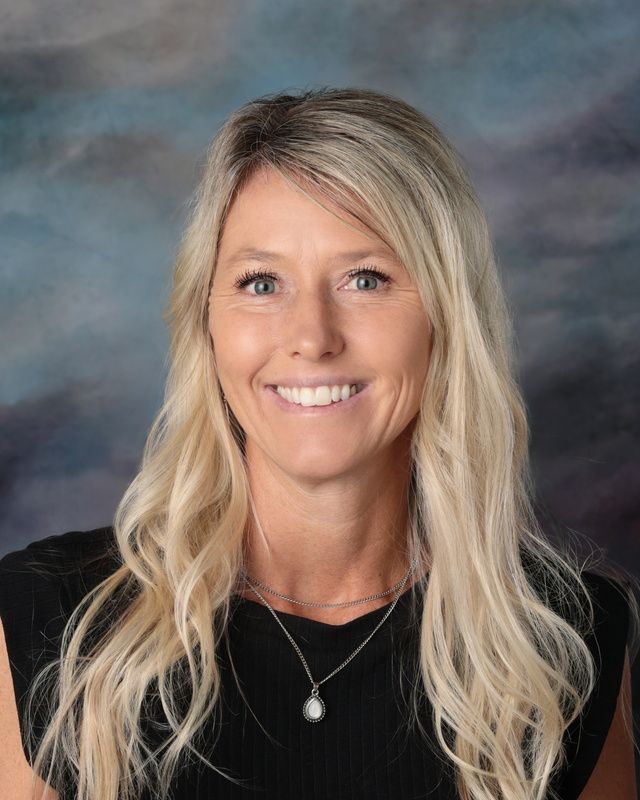 A woman in a white shirt and necklace is smiling in front of a blue background.