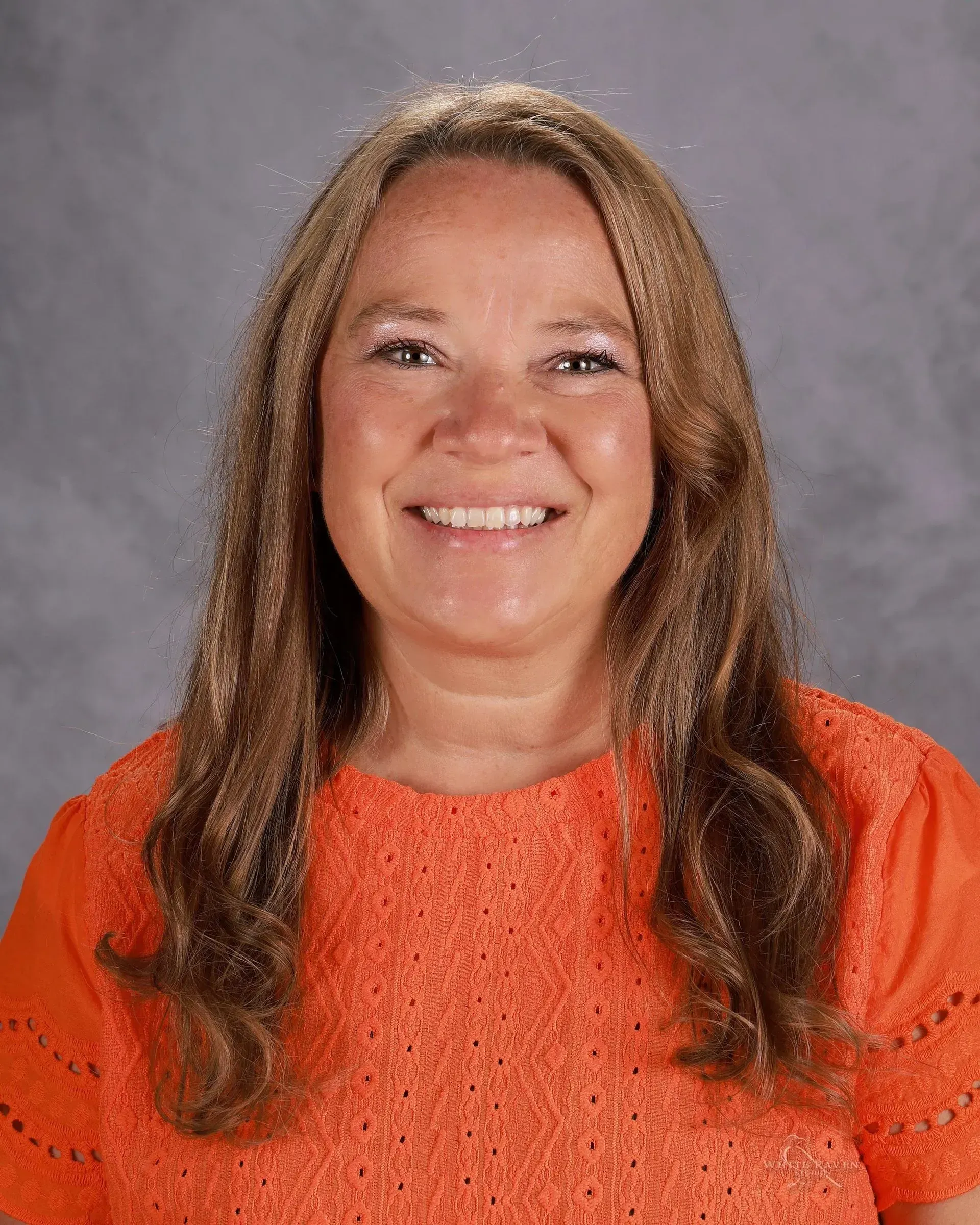 A woman in a pink shirt and necklace is smiling for the camera.
