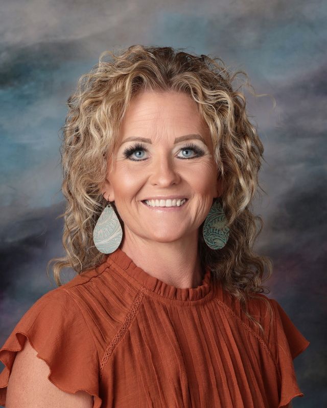 A woman with curly hair is smiling for a picture in front of a blue background.
