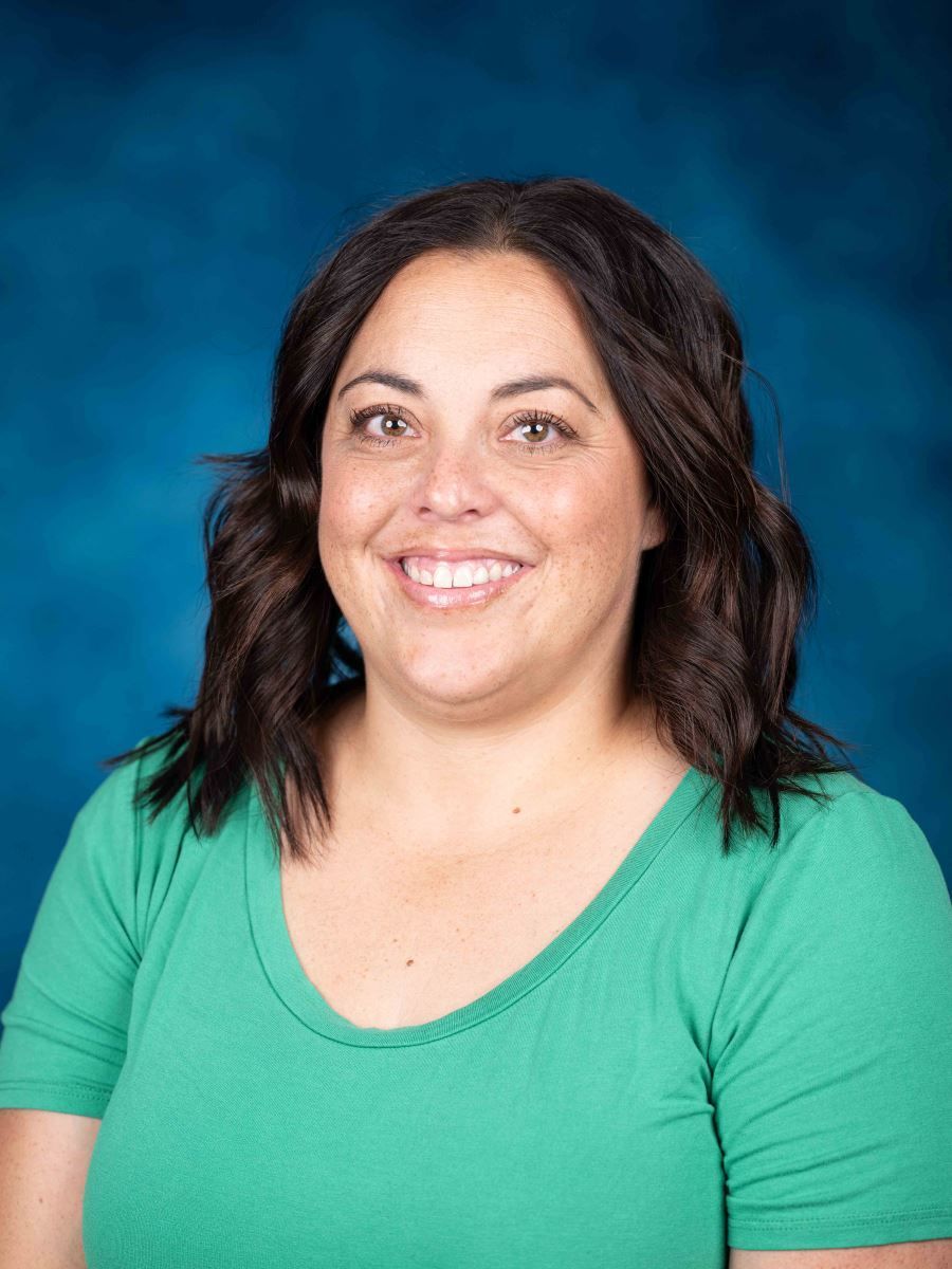 A woman in a green shirt is smiling in front of a blue background.