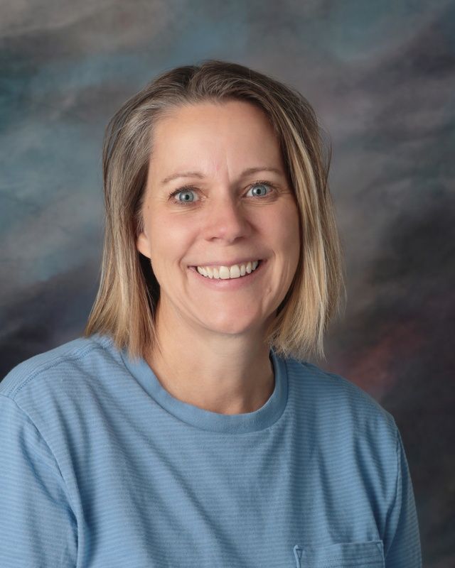 A woman in a pink shirt is smiling in front of a blue background.