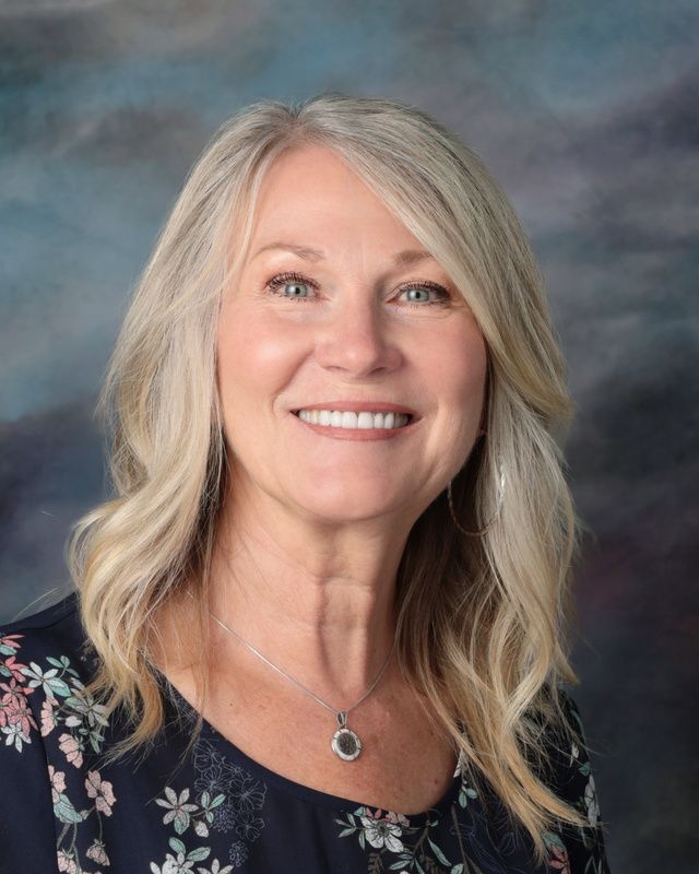A woman in a blue jacket and black top is smiling for the camera.