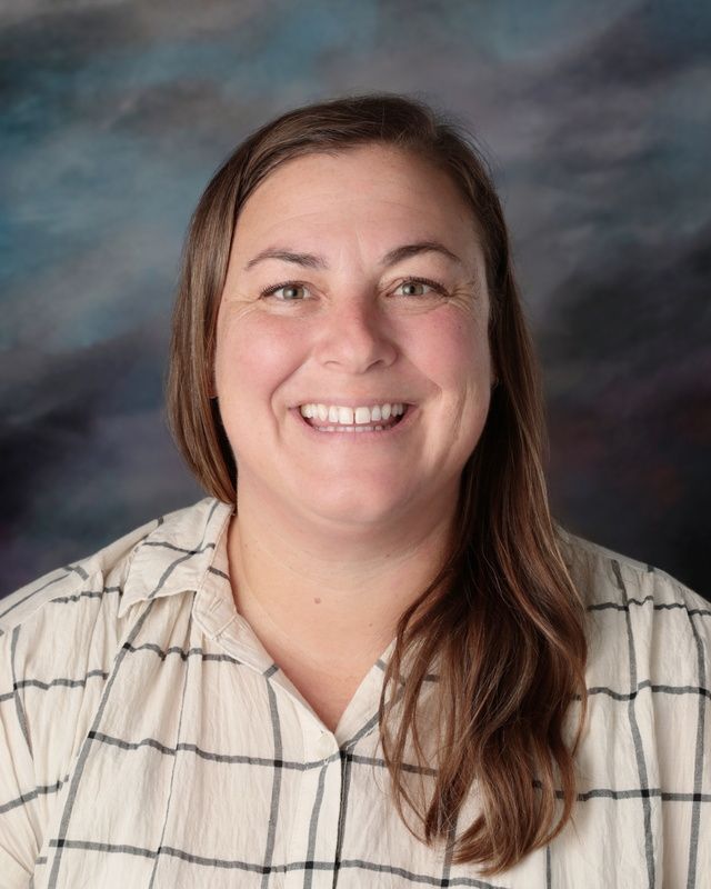 A woman in a red shirt is smiling in front of a blue background.