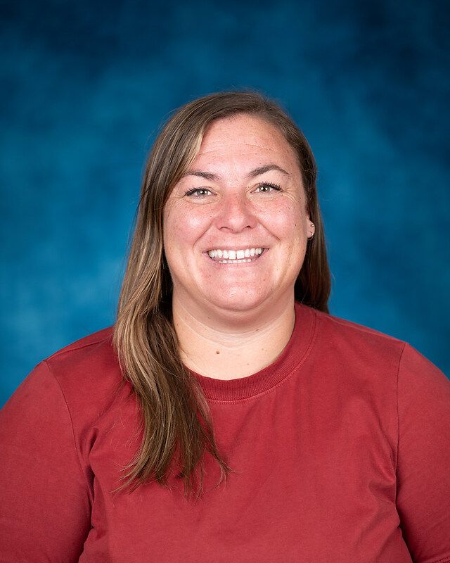 A woman in a red shirt is smiling in front of a blue background.