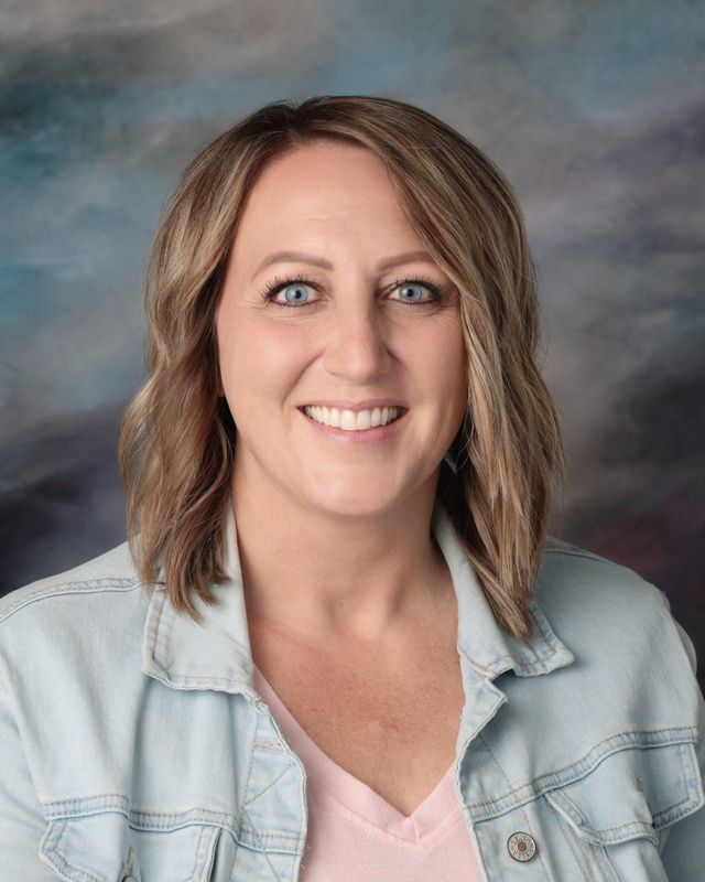 A woman in a green shirt is smiling in front of a blue background.