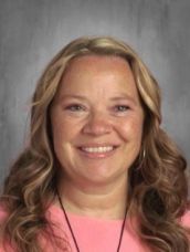 A woman in a pink shirt and necklace is smiling for the camera.