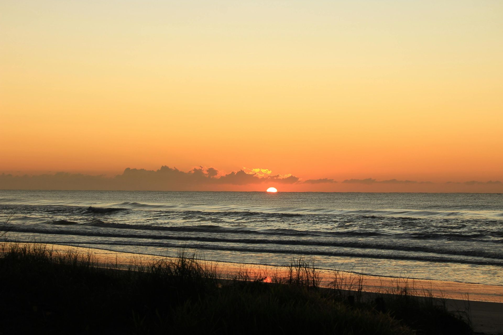 Sunset over ocean, orange sky reflecting on water, beach in foreground.