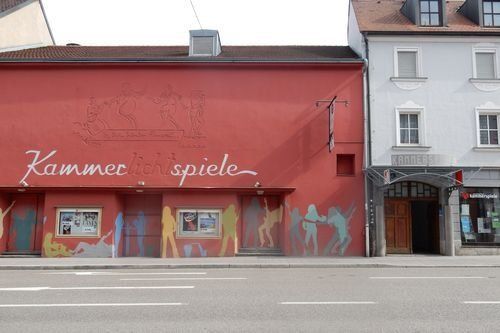 Kammerspiele Ansbach. Fensterloses längliches  Gebäude, daneben mehrstöckiges Haus mit Torbogen.