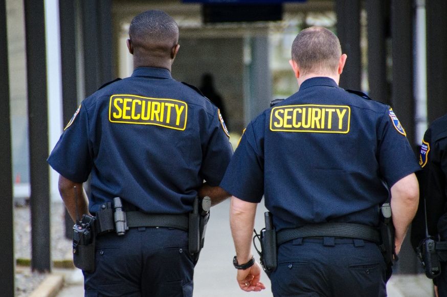Two security guards are walking down a sidewalk.
