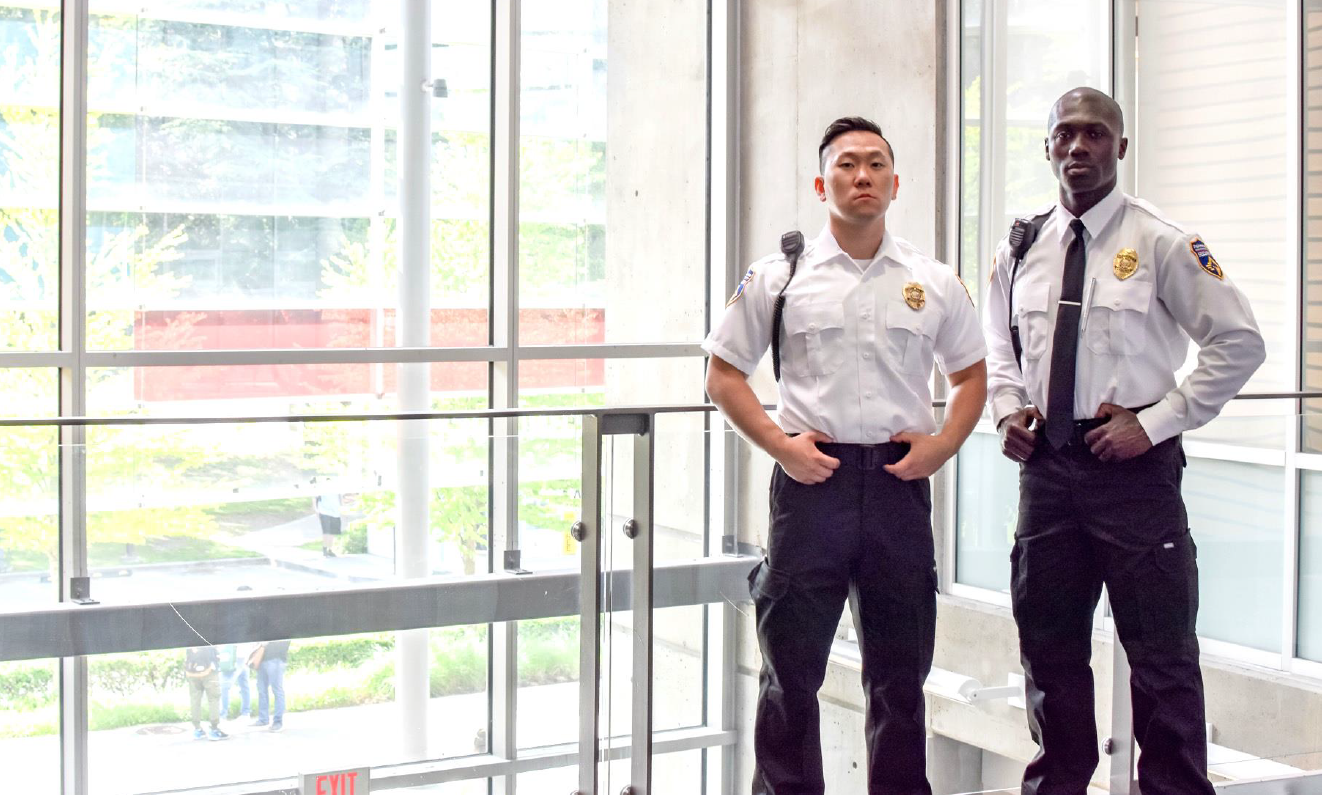 Two security guards are standing next to each other in front of a large window.