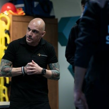 A bald man with tattoos on his arms is wearing a black shirt