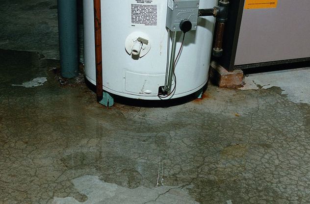A water heater is sitting on a cracked concrete floor in a basement.