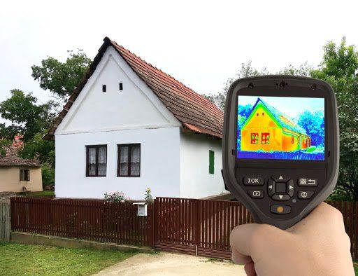 A person is holding a thermal camera in front of a house.