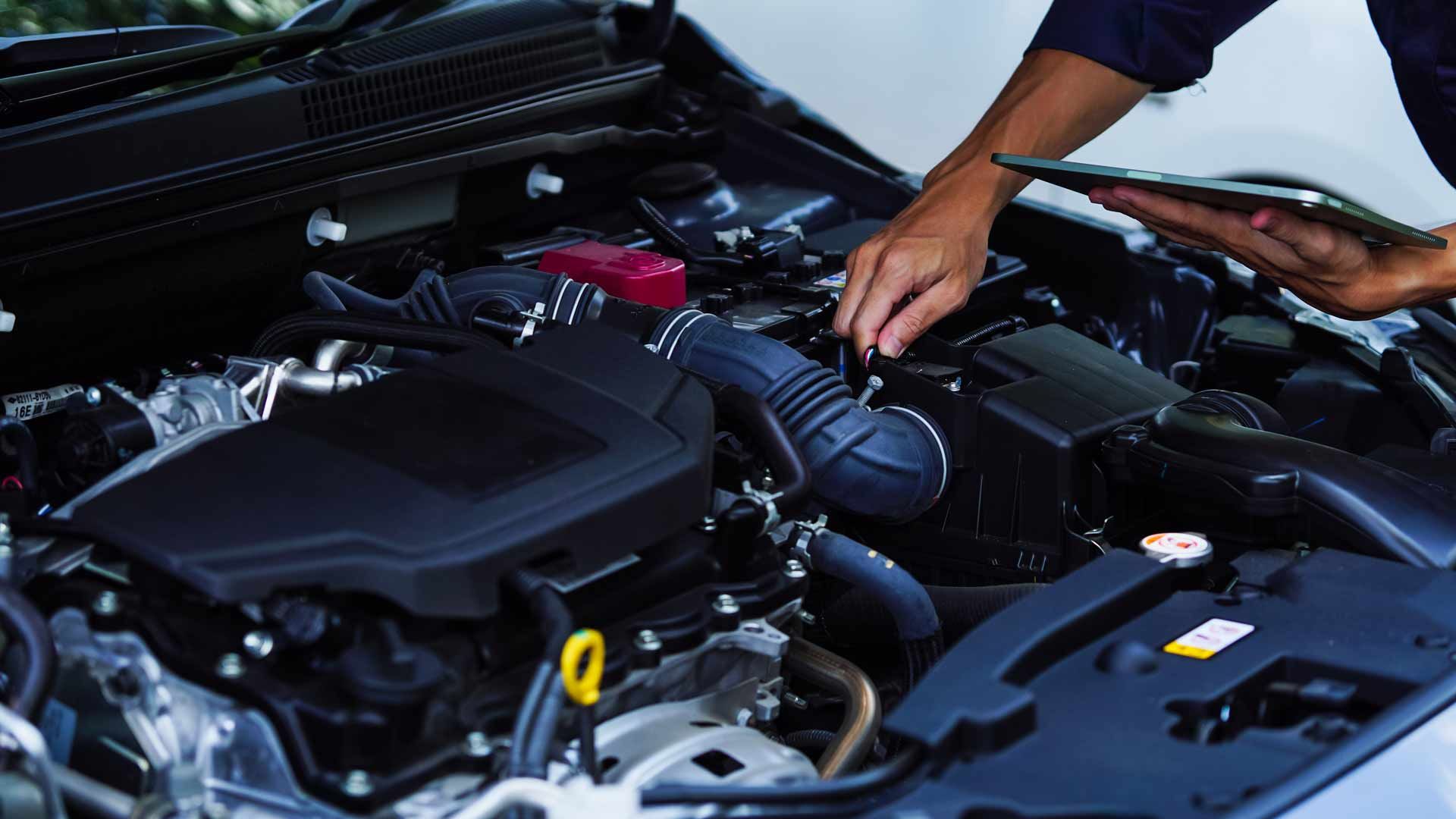 Mechanic working under an open car hood, inspecting the engine bay