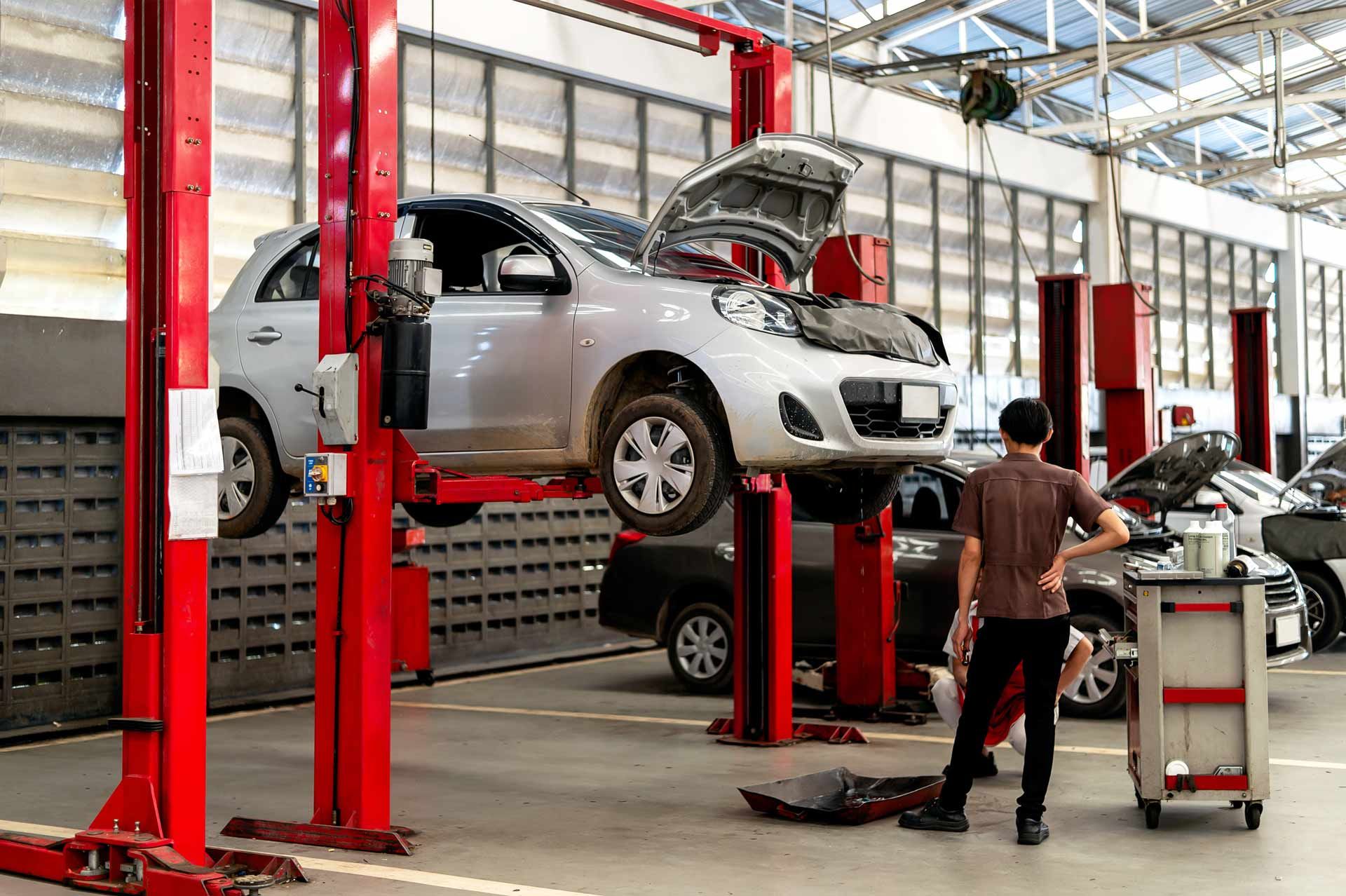 Car lifted on a red automotive hoist while a mechanic works in a garage shop.