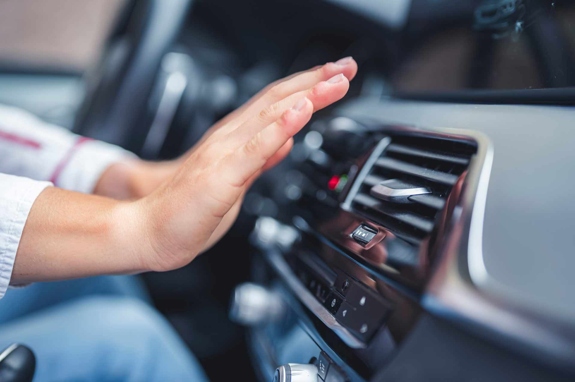 Hand hovering above a car dashboard air vent and controls inside the vehicle