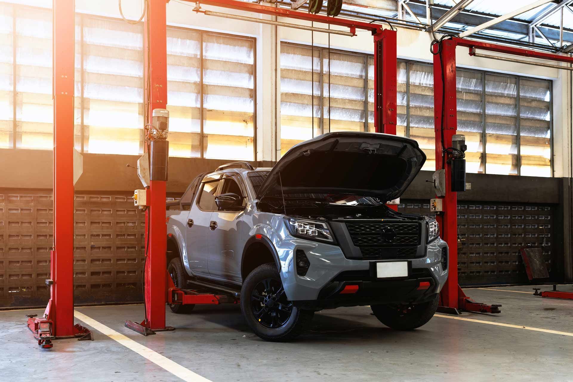 Black SUV on a lift in a garage, with the hood open and sunlight streaming through windows.