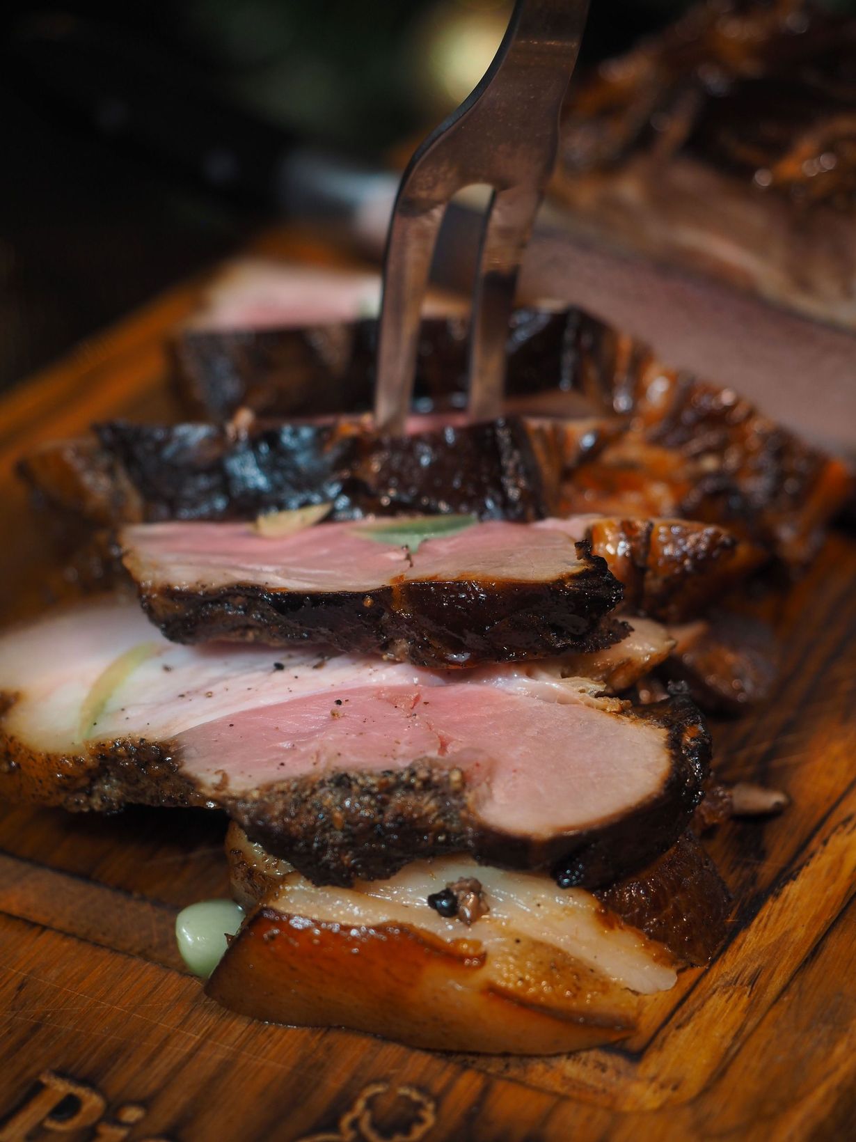 Forchetta che taglia fette di carne arrosto su un tagliere di legno, con una crosticina scura e un interno rosato.