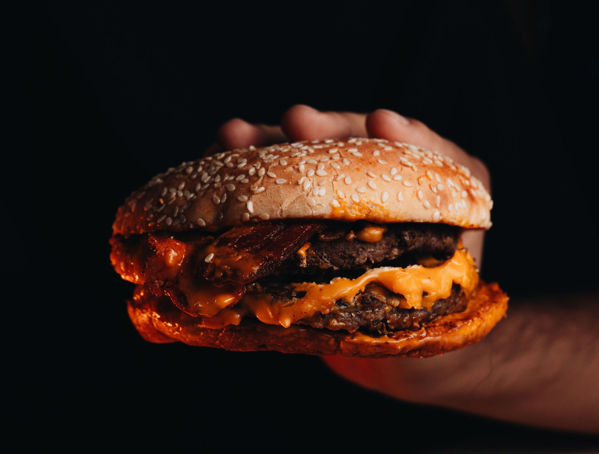 Mano che regge un cheeseburger ricoperto di semi di sesamo su uno sfondo scuro