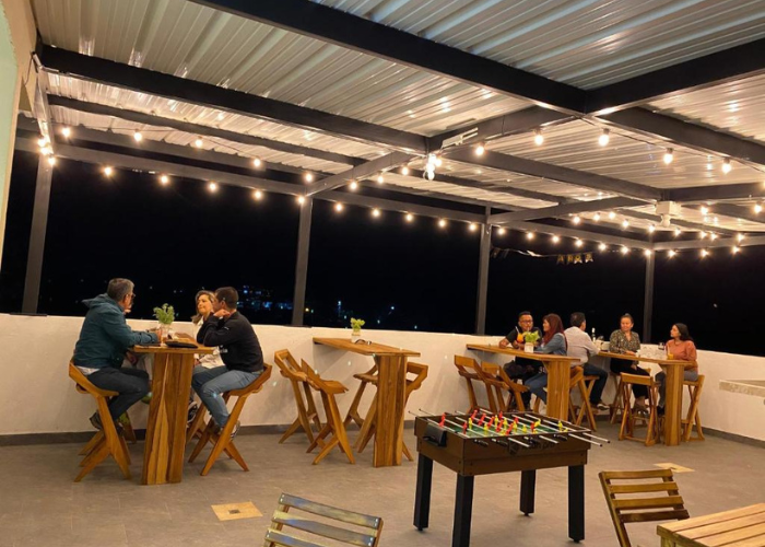 Gente en un bar al aire libre bajo luces de colores, jugando al futbolín y socializando por la noche.