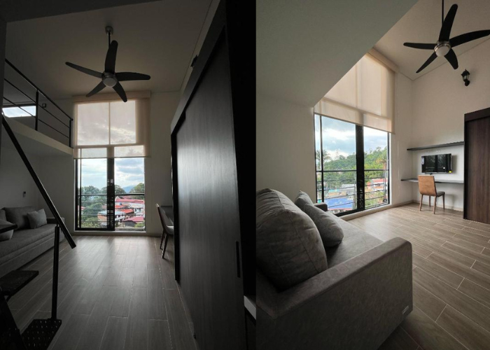 Interior de apartamento tipo loft con grandes ventanales, suelos de madera, un sofá y un ventilador de techo negro.
