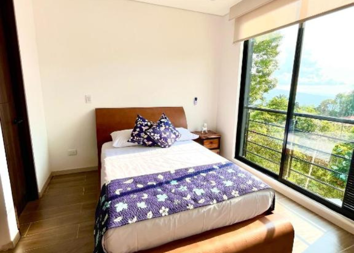 Dormitorio con cama, mesita de noche, amplio ventanal y vista panorámica.