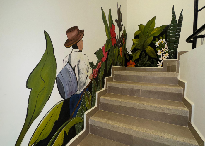 Mural de una persona con una mochila junto a unas escaleras. Hay plantas pintadas en la pared.