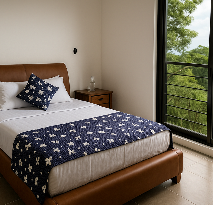 Dormitorio con cama de cuero, ropa de cama blanca y alfombra estampada en color azul, junto a una ventana con vistas.