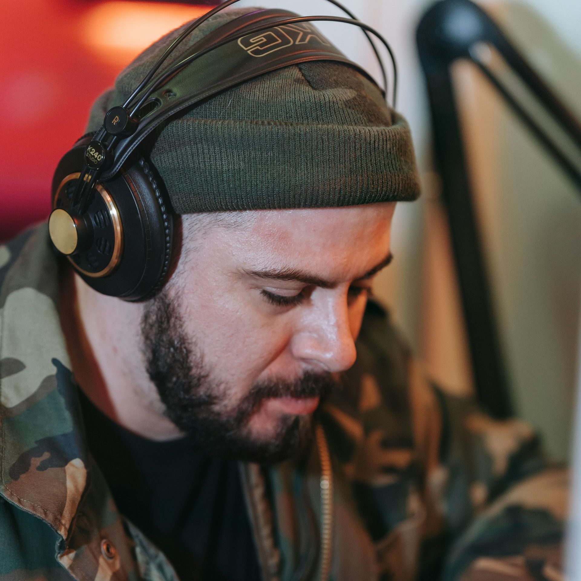Um homem com barba usando fones de ouvido e uma jaqueta camuflada
