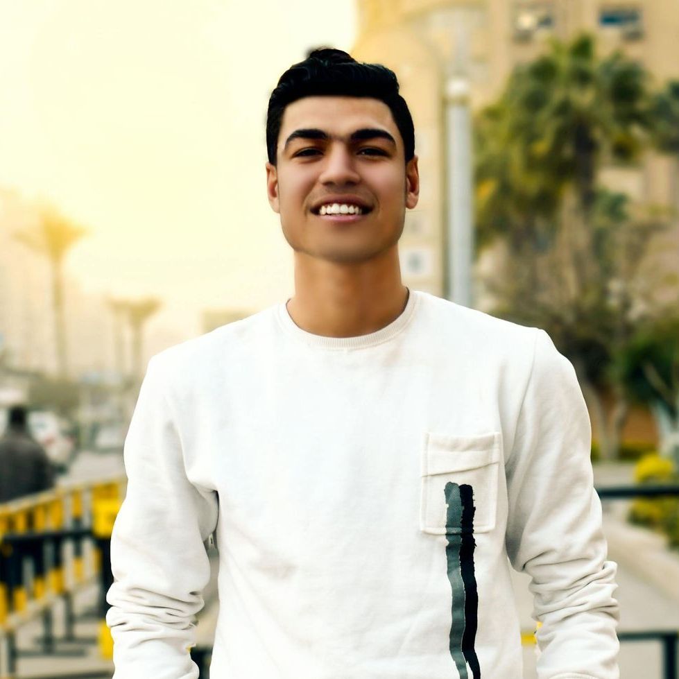 Um jovem vestindo um suéter branco está sorrindo para a câmera