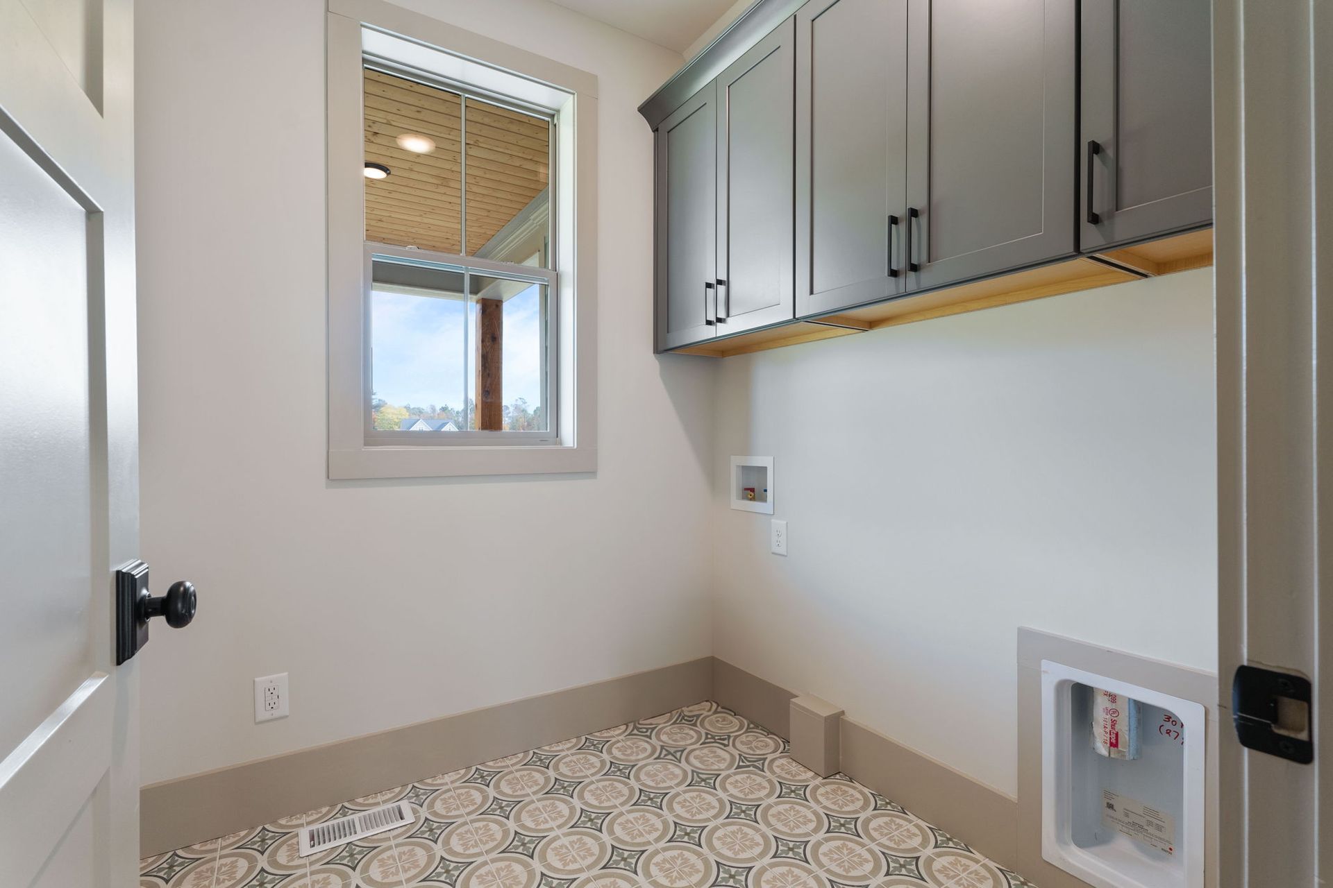 A bespoke laundry room with gray cabinets and a window.
