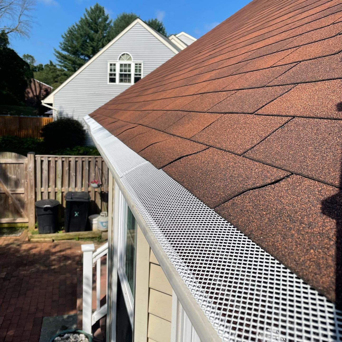 Gutter with white mesh screen on a brown shingled roof, protecting against debris.