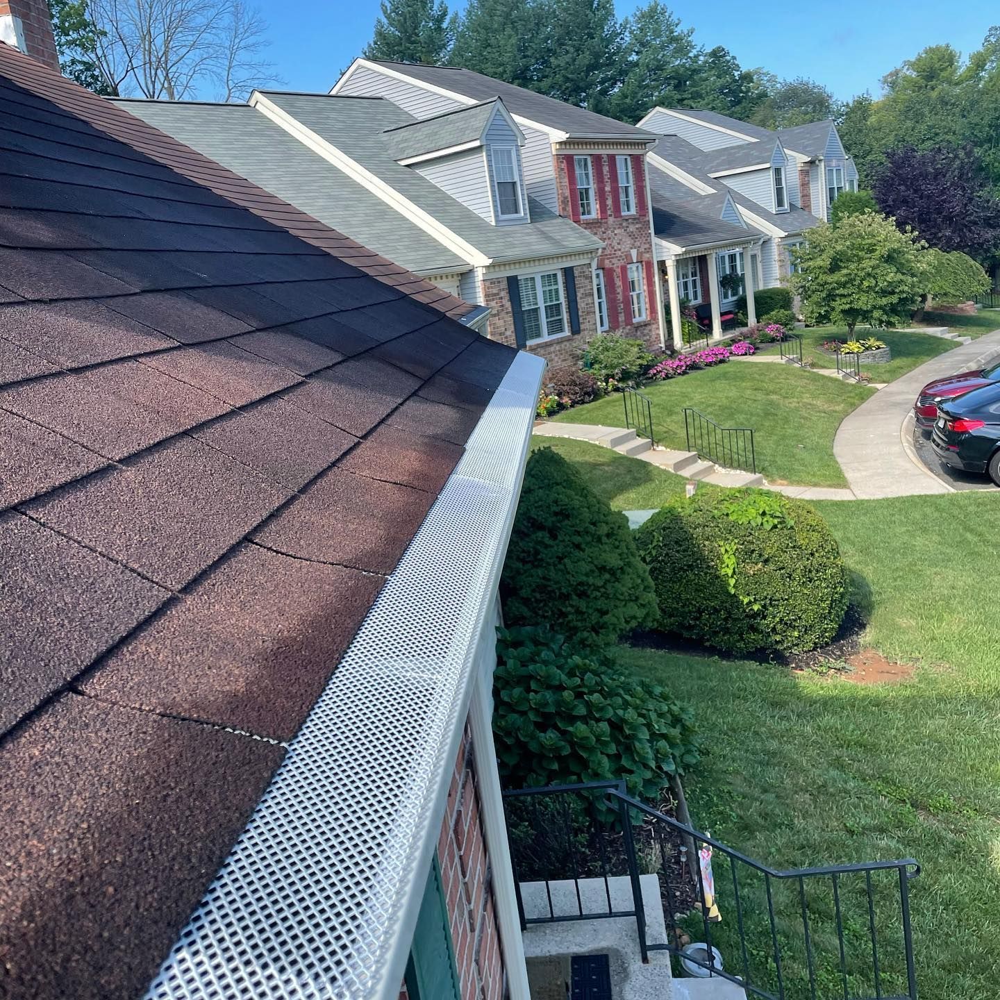 Brown shingled roof with white mesh gutter guard, brick building, suburban houses in the background.