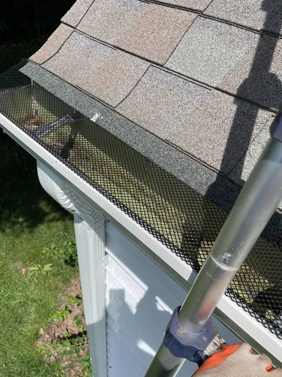 Gutter with mesh screen on a roof, being cleaned with a pole.