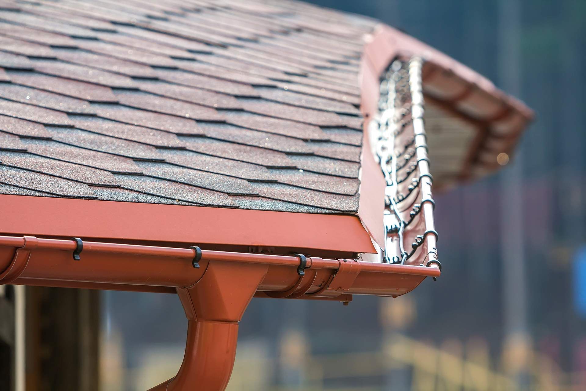 Brown roof with matching gutters; close-up showing shingle detail and a downspout.