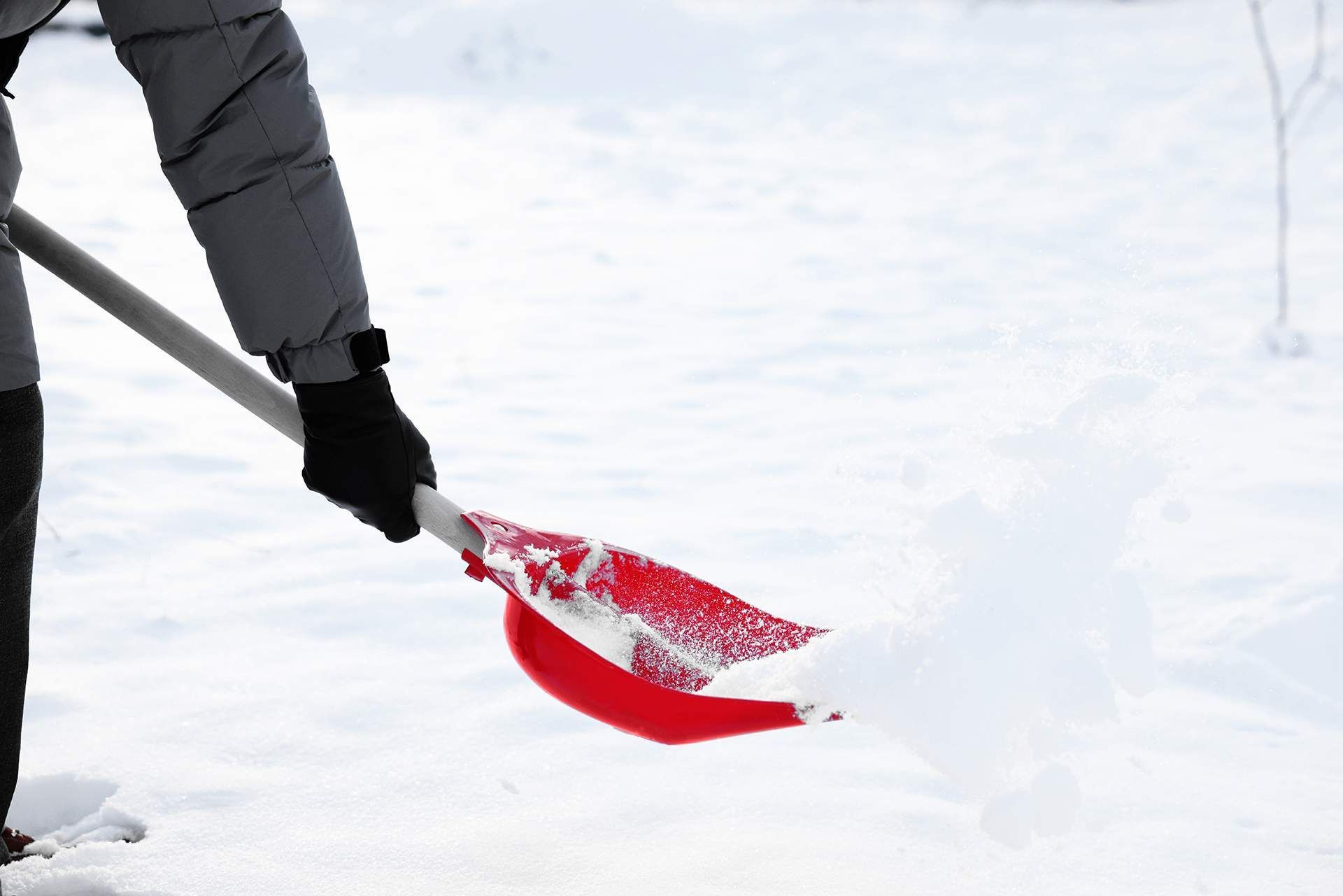 Person shoveling snow with a red shovel, outside in winter.