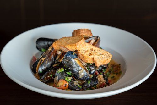 A white plate topped with mussels and bread on a table.