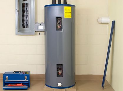 Gray water heater in a utility room with electrical panel, blue toolbox, and broom