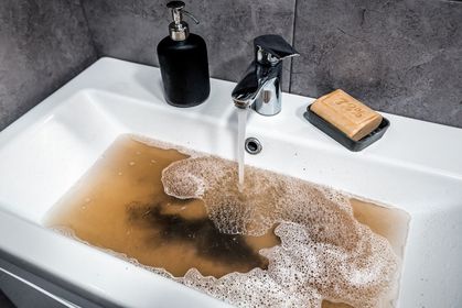 Bathroom sink overflowing with muddy water, soap and sponge on the rim.