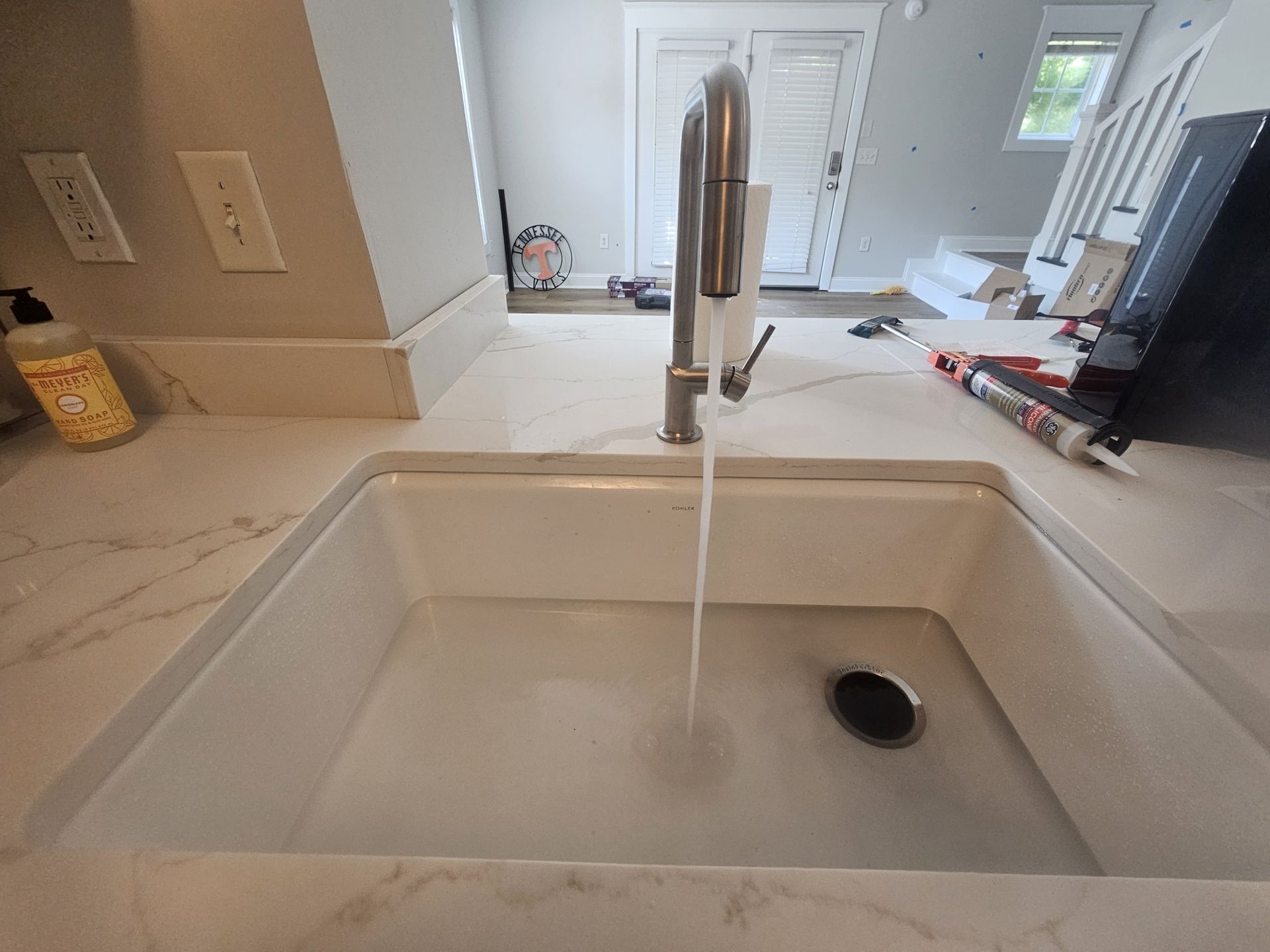 Leaking white PVC pipes under a sink, with water spraying onto the floor.