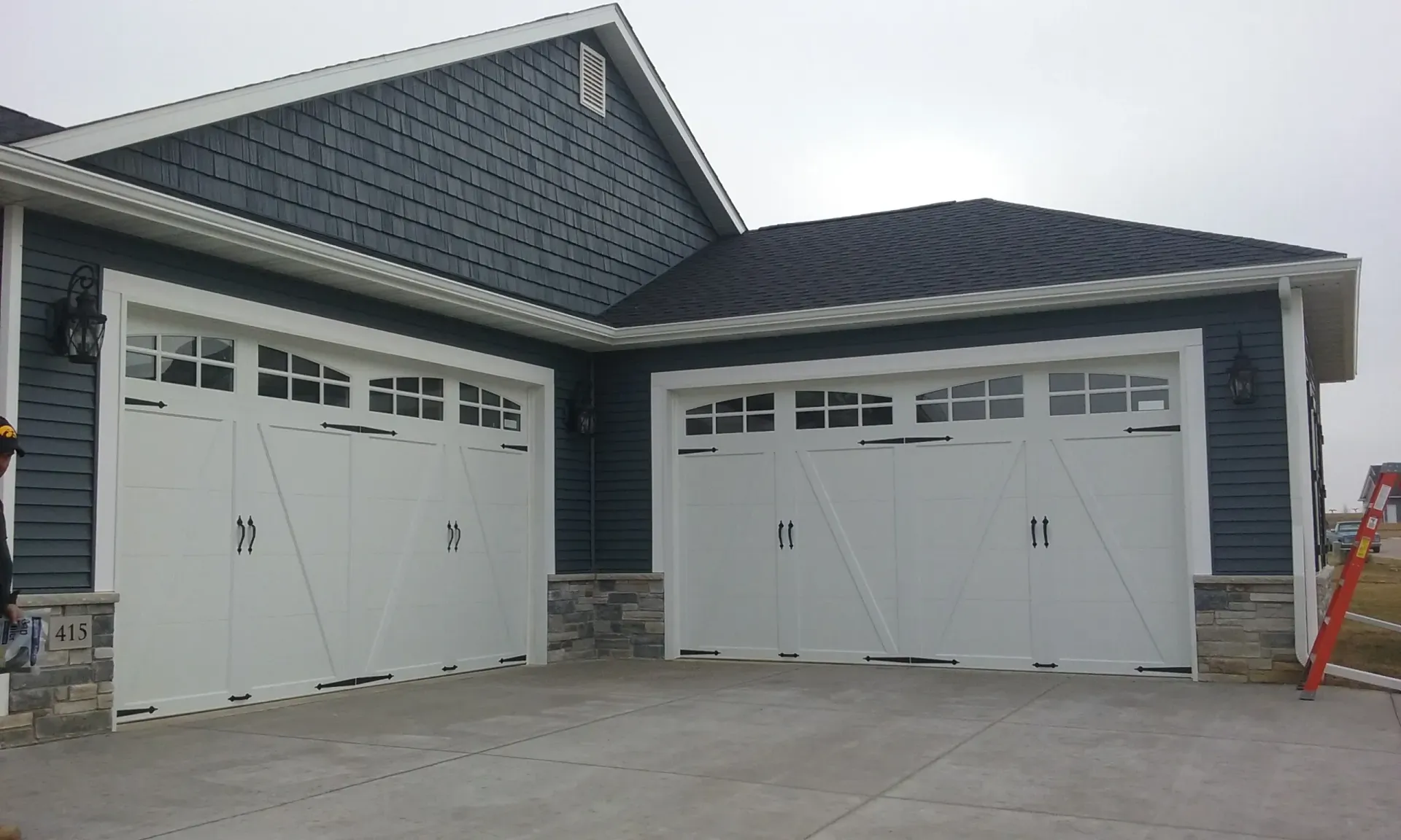 Two white garage doors with black hardware on a house with blue siding and stone accents.