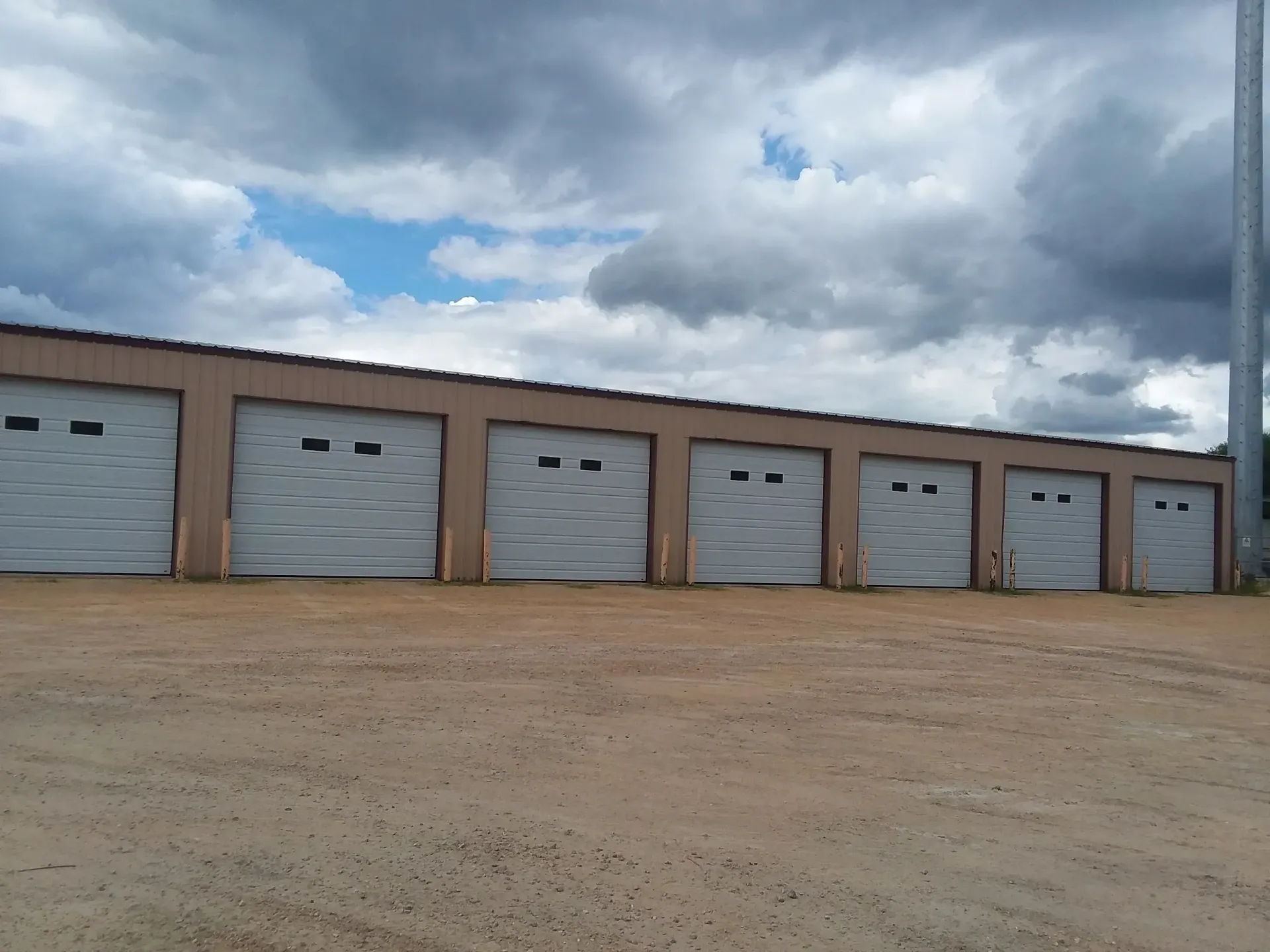 Row of beige storage units under a cloudy sky. A tall, silver tower is visible on the right.